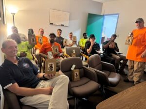 A group of coworkers seated in a casual meeting room, each holding a brown paper bag with a dog image on it.