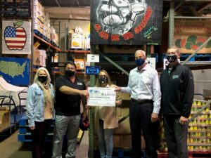 Five people wearing masks stand in a warehouse, handing a large $10,000 check to the Southern Maryland Food Bank.