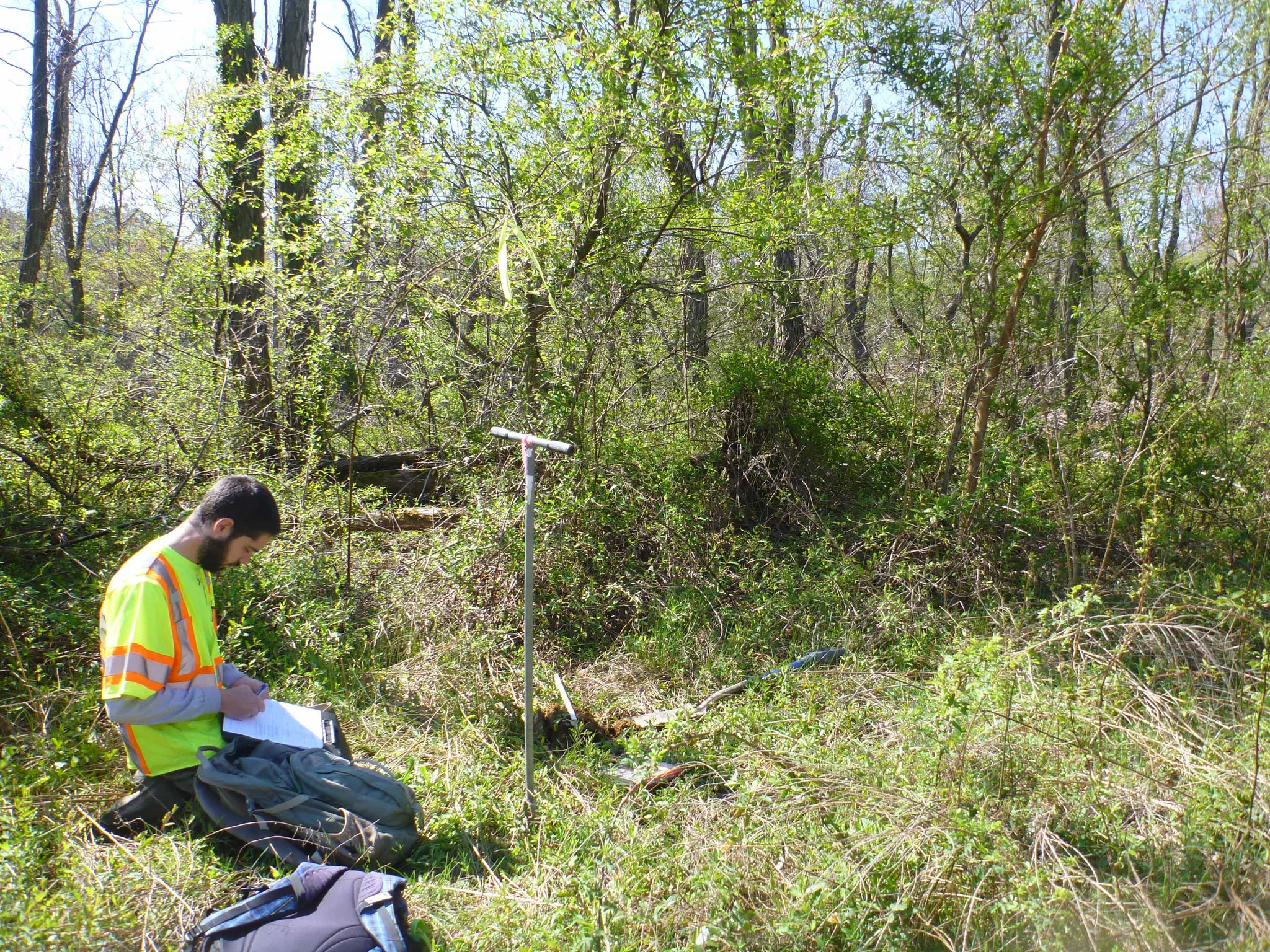Natural_Resources_Services_Page_Image - Geo-Technology Associates, Inc. Worker in a neon safety vest standing in a brushy field reviewing papers with equipment nearby