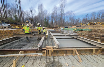 Construction workers in safety vests and hard hats pour and level concrete into wooden formwork for a building foundation at a construction site