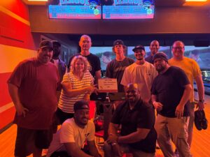 Group of coworkers posing for a photo in a bowling alley with orange lighting and bowling lanes in the background.