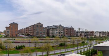 Row of brick apartment buildings with landscaped terraces and a curved road in front of them, under a cloudy sky.